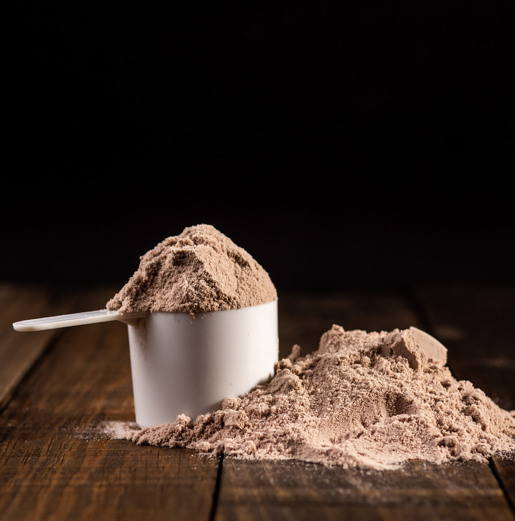 Measuring scoop of whey protein on wooden table to prepare a milkshake. Concept of diet, health and exercise